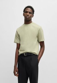 T-shirt verde chiaro con scollo rotondo e maniche corte, realizzato in tessuto morbido. Abbinato a pantaloni neri su misura con cintura.