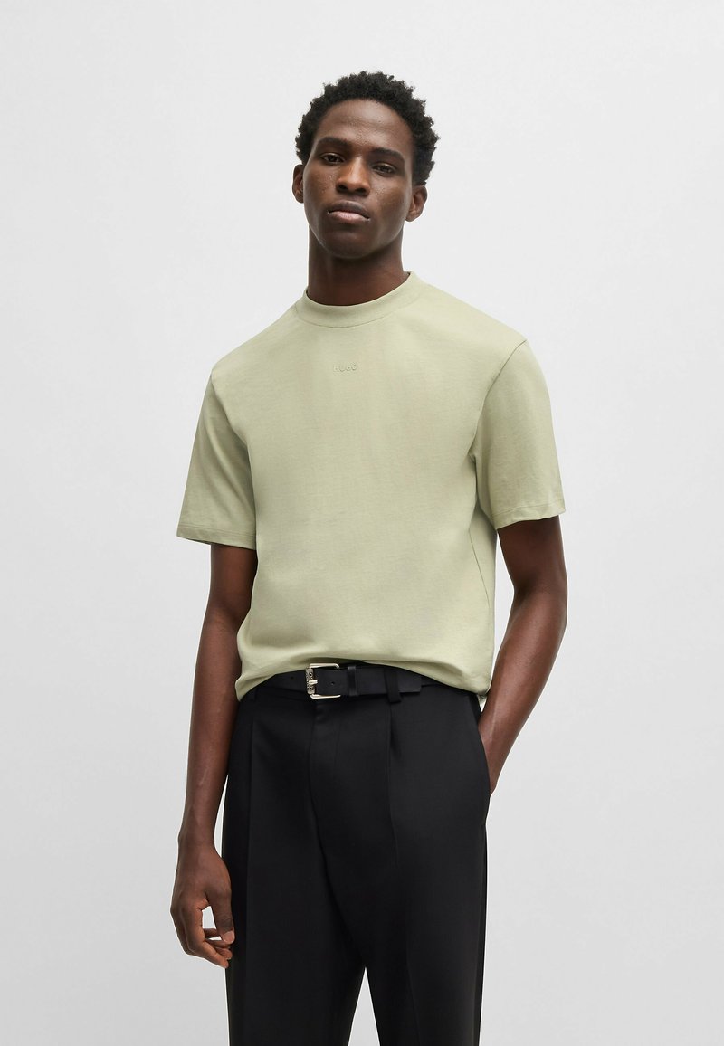 T-shirt verde chiaro con scollo rotondo e maniche corte, realizzato in tessuto morbido. Abbinato a pantaloni neri su misura con cintura.