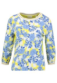 Langarm bloes met blauwe bloemen en gele accenten op een witte achtergrond, met een ronde halslijn en fitted mouwen.