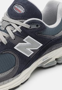 Buty sportowe z ciemnoniebieską i szarościową cholewką z zamszu i siateczki. Posiadają wyraźne srebrne logo "N", szare sznurowadła oraz wygodną białą podeszwę.