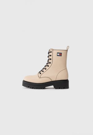 Beige Schnürkampfstiefel mit schwarzer Sohle und Absatz, schwarzen Nähten, Zuglasche und Tommy Jeans-Logopatch am Knöchel.