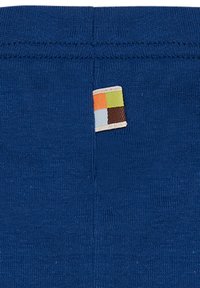 Marineblauwe stof met een zichtbare naad en een klein, multikleurig geweven label met vierkanten in oranje, groen, blauw en bruin.