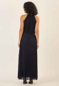 Vestido plisado azul marino con cuello halter, diseño en capas y borde transparente en el dobladillo. Llevado con zapatos de tacón negro.