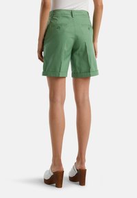 Zelené bavlněné šortky s ohrnutými manžetami, podložené zadními kapsami. V páru s bílými dřevěnými kloboučky na blokovém podpatku.