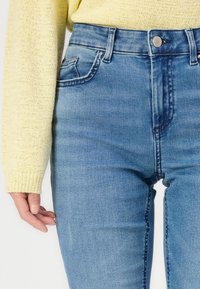 Blue denim jeans with a high waist, five-pocket design, and a light wash. The fabric has a smooth texture and subtle fading details.