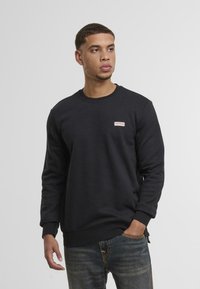 Zwarte sweatshirt gemaakt van een katoenmix, met een ronde hals en lange mouwen. Opvallend klein logo patch op de borst. Draagt met spijkerbroek.