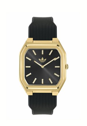 Square black watch face with gold markers and hands, gold bezel, black ridged silicone strap, and Adidas logo at 12 o'clock position.