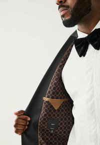 Schwarze Smokingjacke, glattes Material, mit einem aufwändigen braun-schwarzen Futter und einem Etikett in der Innentasche.