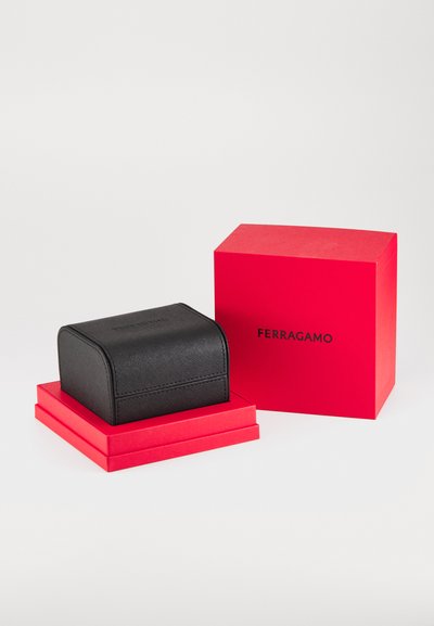 Boîte à bijoux en cuir noir avec une surface texturée, placée sur une base empilée rouge. Comprend une boîte-cadeau rouge audacieuse avec le logo "FERRAGAMO".