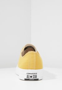 Baskets en toile jaune à design bas, semelle en caoutchouc blanche et marquage "Converse All Star Renew" sur le talon. Détails cousus visibles.