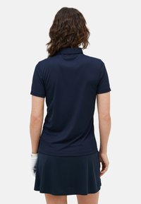 Marineblaues Poloshirt mit kurzen Ärmeln, Kragen-Design, glatte Textur, kombiniert mit einem passenden Rock. Fokus auf einem schlanken, sportlichen Look.
