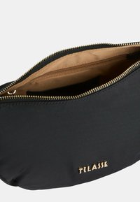 Borsa nera in nylon con una cerniera dorata, caratterizzata da un esterno liscio e un rivestimento interno beige. Marchio noto impresso in oro.