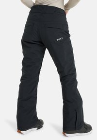 Zwarte sneeuwbroek met een relaxte pasvorm, voorzien van een Roxy-logo op de achterkant, een gestructureerde stof en ritssluitingen aan de zijkant voor ventilatie.