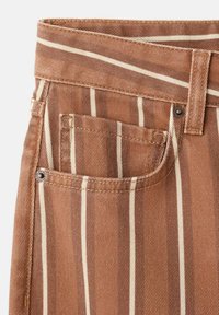 Pantaloni di denim marrone con strisce verticali bianche, dotati di tasca frontale, passante per cintura e dettagli in rivetti metallici.