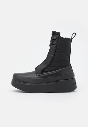 Botte noire montante à plateforme avec semelle épaisse, lacets à l'avant, cheville rembourrée et languette à l'arrière, présentée sur un fond neutre.