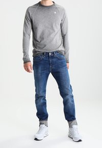 Grå långärmad tröja med rund halsringning, blå jeans och vita sneakers. Tröjan har en subtil textur; jeansen har klassisk passform med uppvikta muddar.