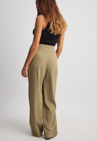 Visoke hlače širokega kroja iz olivno zelene tkanine z gladko teksturo. Imajo plise na hrbtni strani in prilagojen kroj.