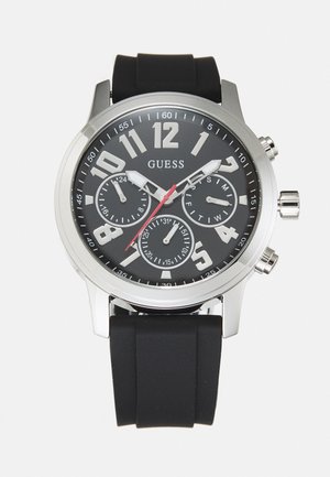 Montre avec bracelet en caoutchouc noir, boîtier en acier inoxydable argenté, cadran noir, grands chiffres blancs et trois sous-cadrans. Accents rouges et poussoirs chromés.