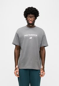 Γκρι βαμβακερό t-shirt με στρογγυλή λαιμόκοψη και κοντά μανίκια, με το λογότυπο "new balance ATHLETICS" σε λευκό, συνδυασμένο με τιρκουάζ φόρμα.