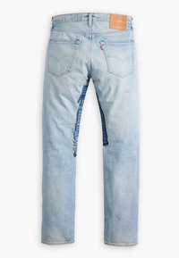 Jean en denim bleu clair vu de dos avec deux poches et une grande déchirure verticale sur la jambe droite laissant apparaître un denim plus foncé en dessous.