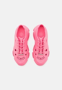 Sneaker rosa brillante realizzati in un materiale testurizzato simile alla gomma, dotati di numerosi fori di ventilazione e lacci piatti con un accento metallico.