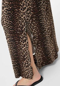Maxikjol i leopardtryck med plisserad textur, som har en vågig nederkant och en sidoklyvning. Huvudfärgerna är beige, svart och brun.