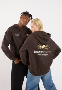 Brown hoodies featuring a front graphic with "The Code of Cool" and a back design with playful emojis and "TRANSFORMING pixels into designs."