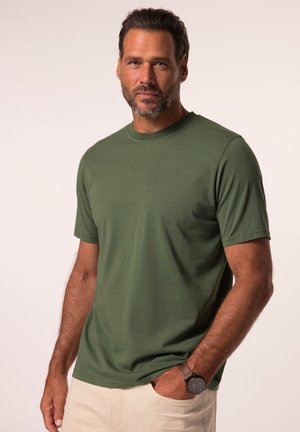 Groene T-shirt met korte mouwen van katoen met een ronde hals. De drager heeft een horloge om, en de stof ziet er glad en lichtgewicht uit.