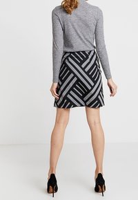 Jupe noire et grise à motifs avec des lignes diagonales, associée à un haut ajusté gris à manches longues et des chaussures noires à talons.