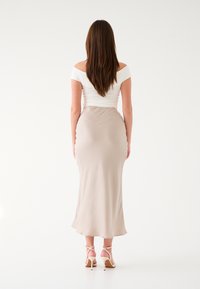 Top bianco scollato sulle spalle abbinato a una gonna aderente beige che arriva fino alla caviglia, caratterizzata da una texture liscia e un design minimal.