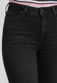 Jeans in denim nero con un design aderente, dotati di vita media, tasche frontali e hardware standard. Texture liscia e dettagli minimi.