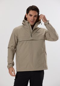 Veste pullover imperméable beige avec une poche zippée à l'avant, une capuche ajustable et des poignets élastiques. Elle se distingue par un design élégant et un tissu léger.