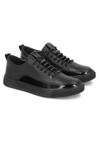 Zapatillas negras de cuero liso con acentos brillantes, punta redonda y suela de goma plana; cuentan con cierre de cordones y tiradores en el talón.