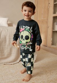 Felpa scura con grafica vivace di un teschio e scritta, abbinata a pantaloni jogger con motivo in bianco e nero. Materiale morbido, vestibilità comoda.