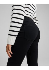 Svarta denimjeans med en figurnära design och bakfickor, ihopparade med en vit tröja med svarta horisontella ränder.