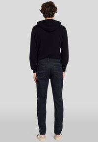 Zwarte hoodie met lange mouwen, gecombineerd met donkerblauwe denim jeans met achterzakken en subtiele stiksels.