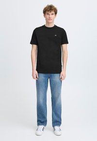 Tricou negru din bumbac cu guler rotund, detaliu logo pe față, asortat cu blugi straight-leg de un albastru deschis și pantofi sport albi.