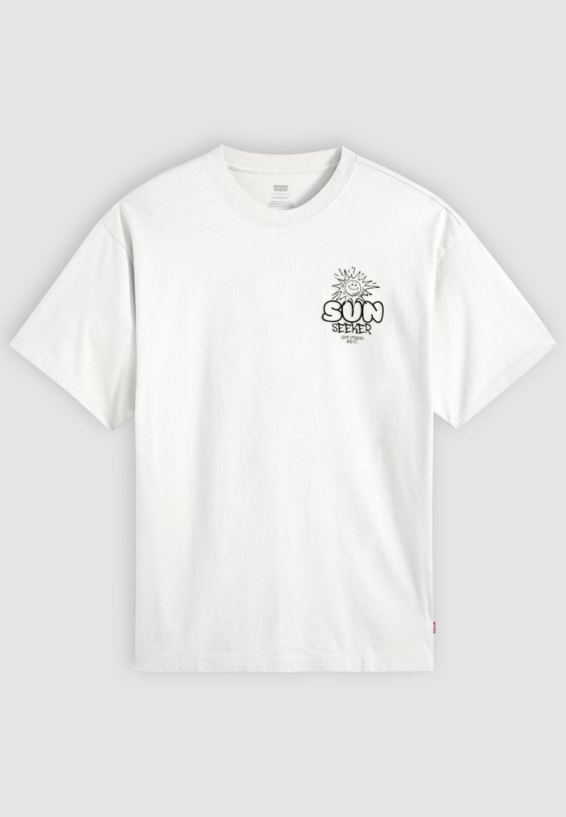Hvid T-shirt med korte ærmer med sort grafik af en smilende sol og ordene "SUN SEEKER" på øverste venstre bryst.