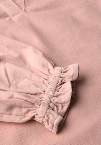 Rosa Stoffoberteil mit strukturiertem Material, gerafften Ärmeln mit elastischen Bündchen und dezentem Rippmuster.