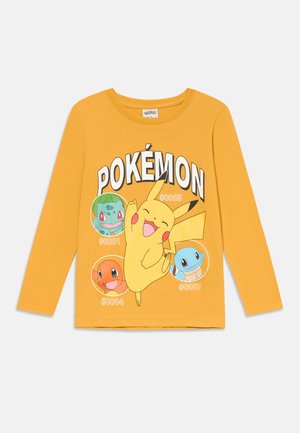 Dzeltena garām piedurknēm T-kreklā ir attēlots Pikachu, kā arī trīs Pokémoni (Bulbasaur, Charmander, Squirtle) ar skaitļiem. Apģērbs izgatavots no kokvilnas auduma.