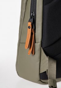 Zaino verde oliva con tessuto texture, dotato di dettagli neri, una zip con maniglie in pelle beige e una cinghia laterale.