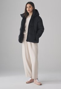 Giacca imbottita nera con cappuccio e design trapuntato. Abbinata a una felpa color crema e pantaloni crema coordinati. Sneakers rosa chiaro.