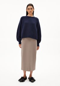 Marineblauwe gebreide trui, beige rok tot de knie en zwarte schoenen met franjes. Losse pasvorm en ribbelstructuur op de trui.