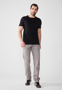 Černé tričko s krátkým rukávem typu henley se třemi knoflíky, kombinované se světlými šedými džíny a černými teniskami. Minimalistický design a uvolněný střih.