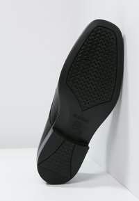 Suela de zapato de goma negra con una superficie texturizada, que presenta un agarre con patrón y un logo de GEOX. Forma ligeramente contorneada para mayor comodidad.