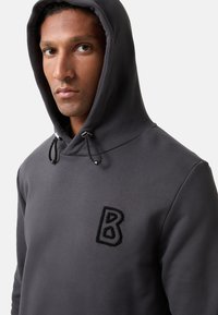 Grijze hoodie met een trekkoordhoed, voorzien van een zwarte geborduurde 'B' op de borst. Gemaakt van een zachte stof, gladde textuur en een relaxte pasvorm.