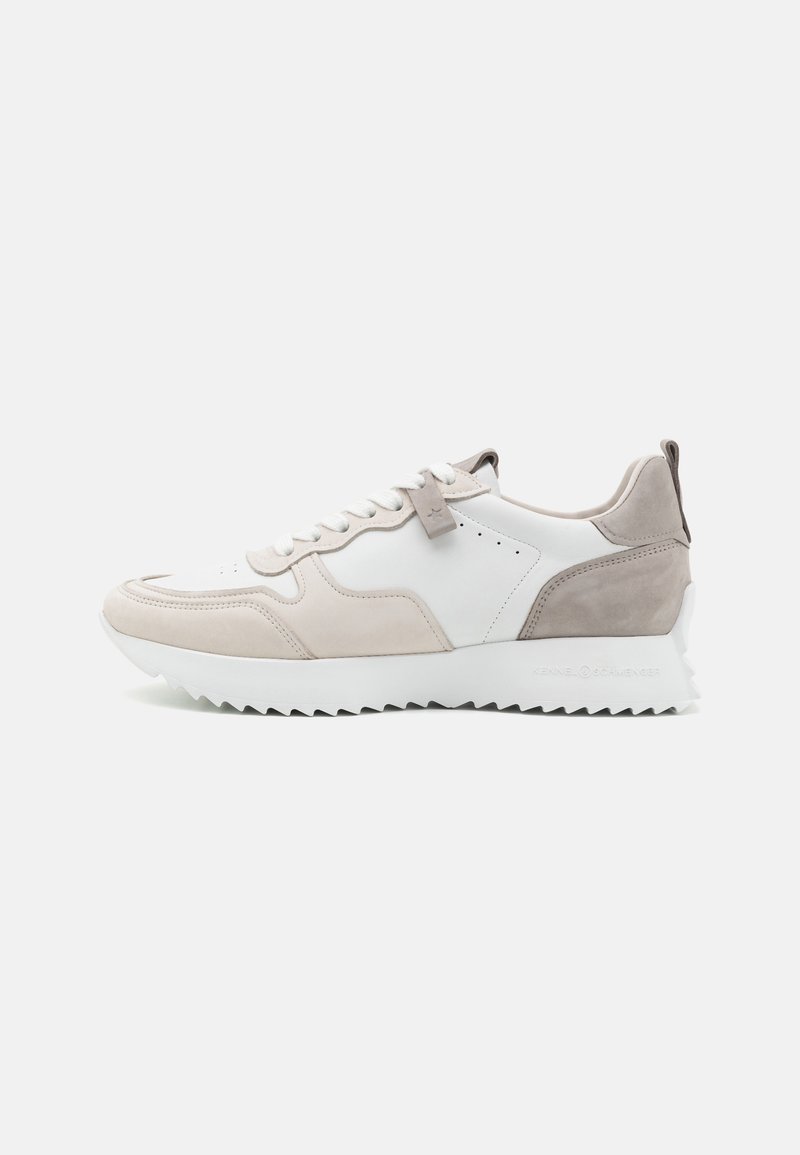 Baskets basses beige clair et blanches avec semelle en zigzag, fermeture à lacets sur le devant et accents en daim, présentées de profil sur un fond blanc.