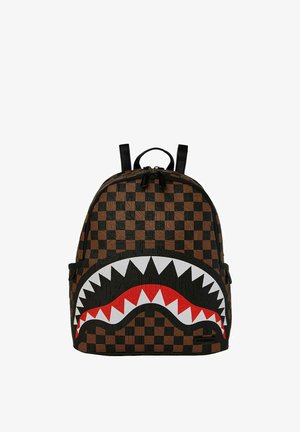 Zaino con motivo a scacchi marrone e nero, caratterizzato da un design prominente di una bocca di squalo in bianco e rosso. Realizzato in materiale resistente, chiusura con cerniera.