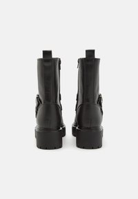 Botas de tobillo de cuero negro con suela gruesa, cremalleras laterales y una correa decorativa en el exterior. Textura suave con detalles mínimos.