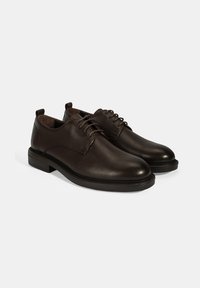 Bruine leren schoenen met een gestructureerde afwerking, ronde neus en vetersluiting. Stevige zwarte rubberen zool met een lichte hak.